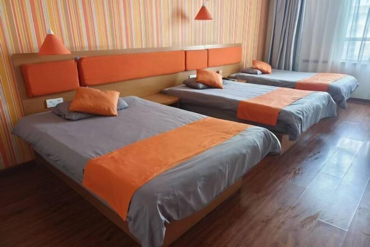 Una habitación de hotel con tres camas, piso de madera y papel tapiz a rayas.