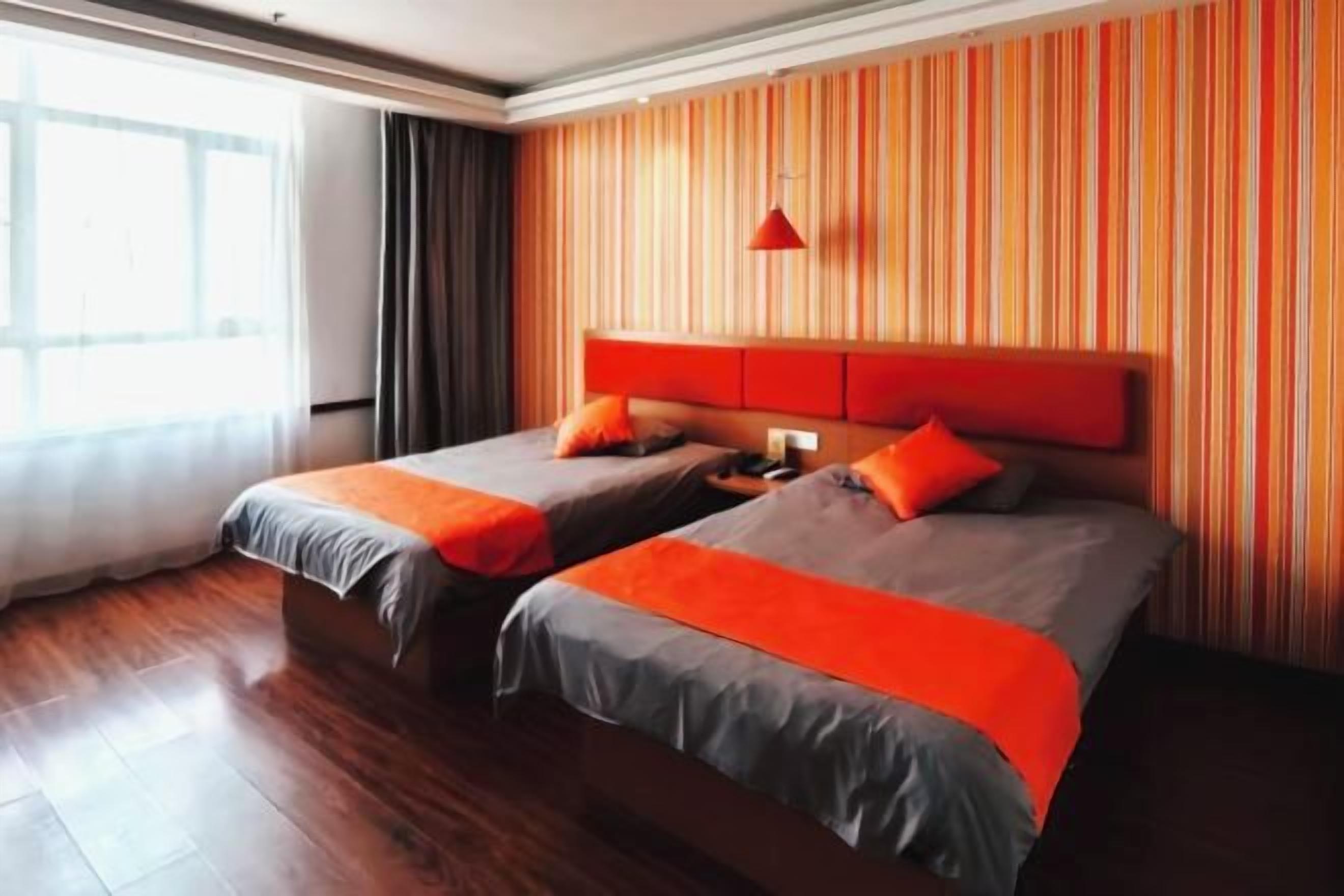 A hotel room with two beds, wooden flooring, a striped wall, and a red pendant light.