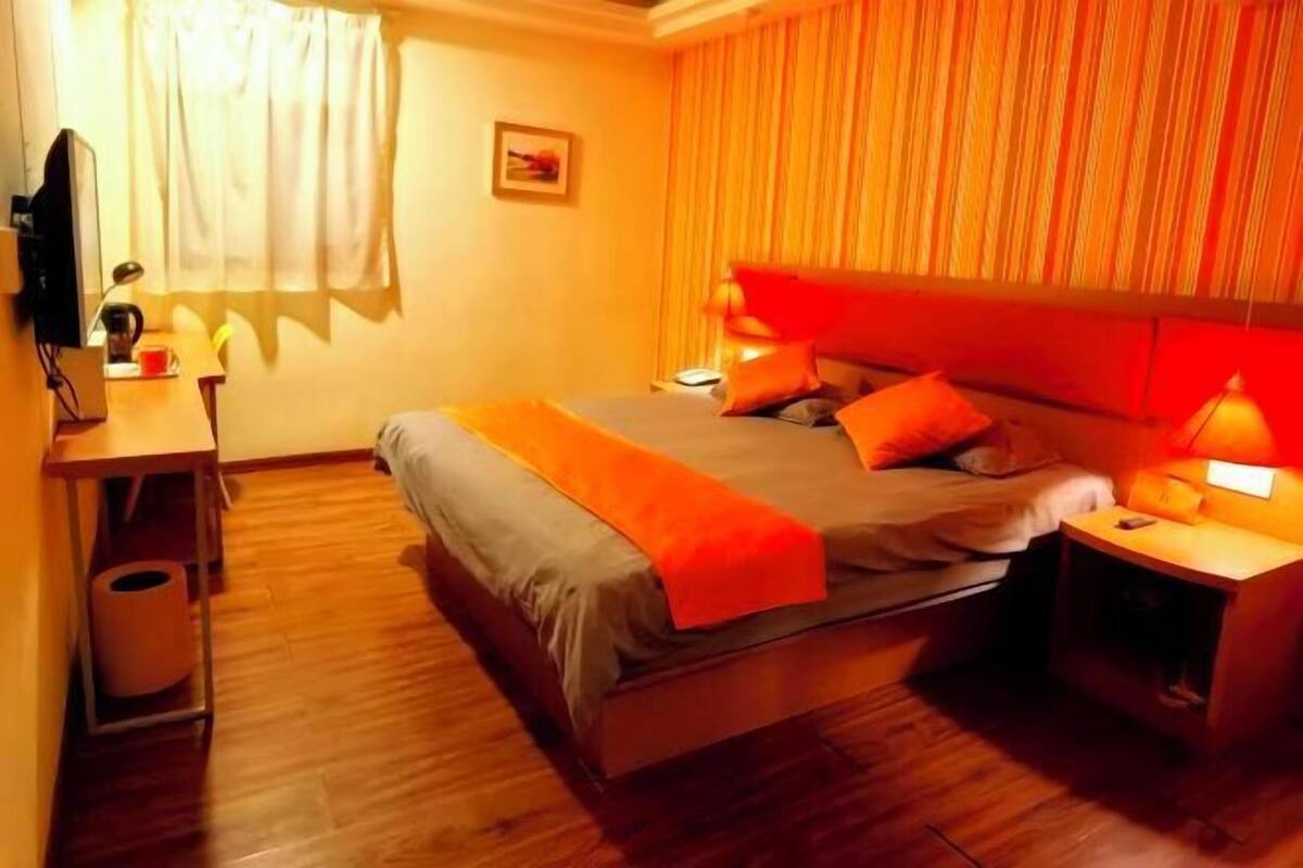 Un dormitorio con cama, mesitas de noche, escritorio, silla, televisor y ventana con cortinas.
