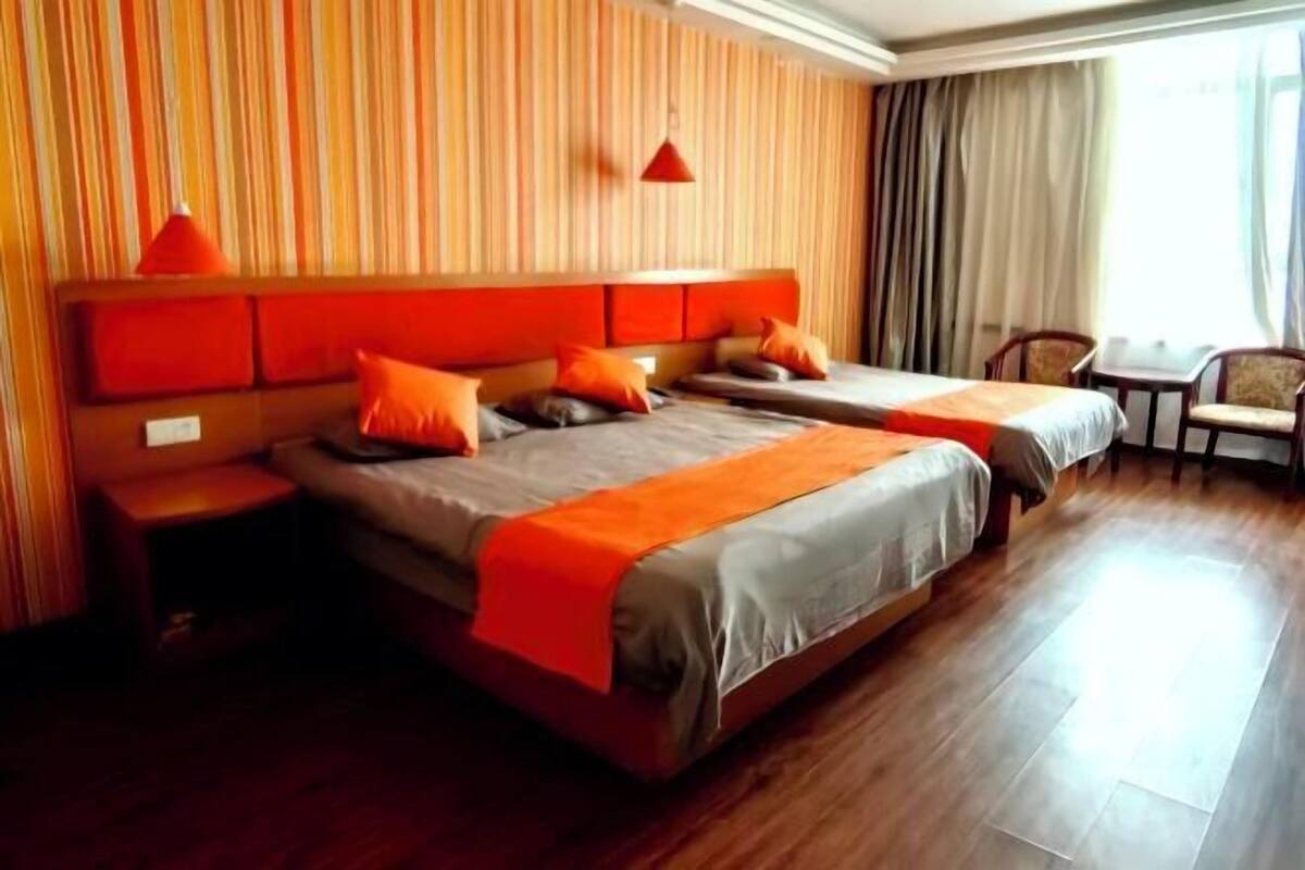 Habitación de hotel con dos camas, piso de madera, pared a rayas y una ventana con cortinas.