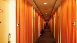 Un pasillo de hotel con paredes a rayas y puertas, suelo alfombrado e iluminación empotrada en el techo.
