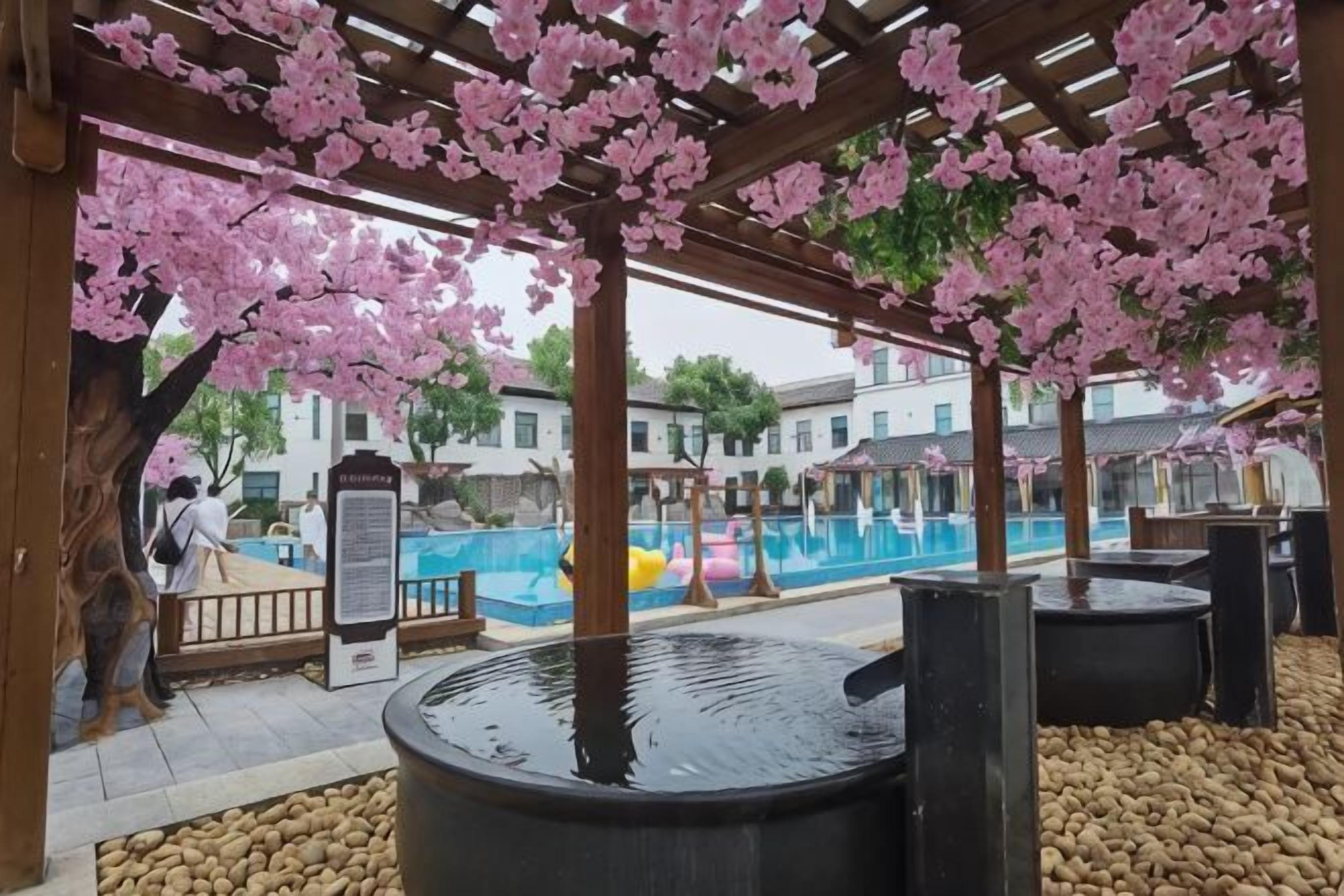 A covered outdoor area with a pool, wooden pergola, and cherry blossoms.