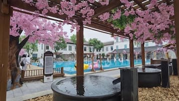 Un espacio al aire libre cubierto con piscina, pérgola de madera y flores de cerezo.