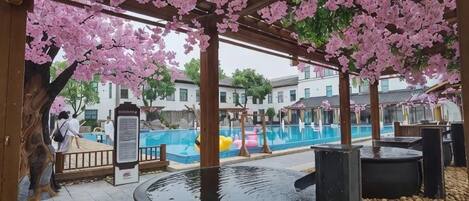 A covered outdoor area with a pool, wooden pergola, and cherry blossoms.