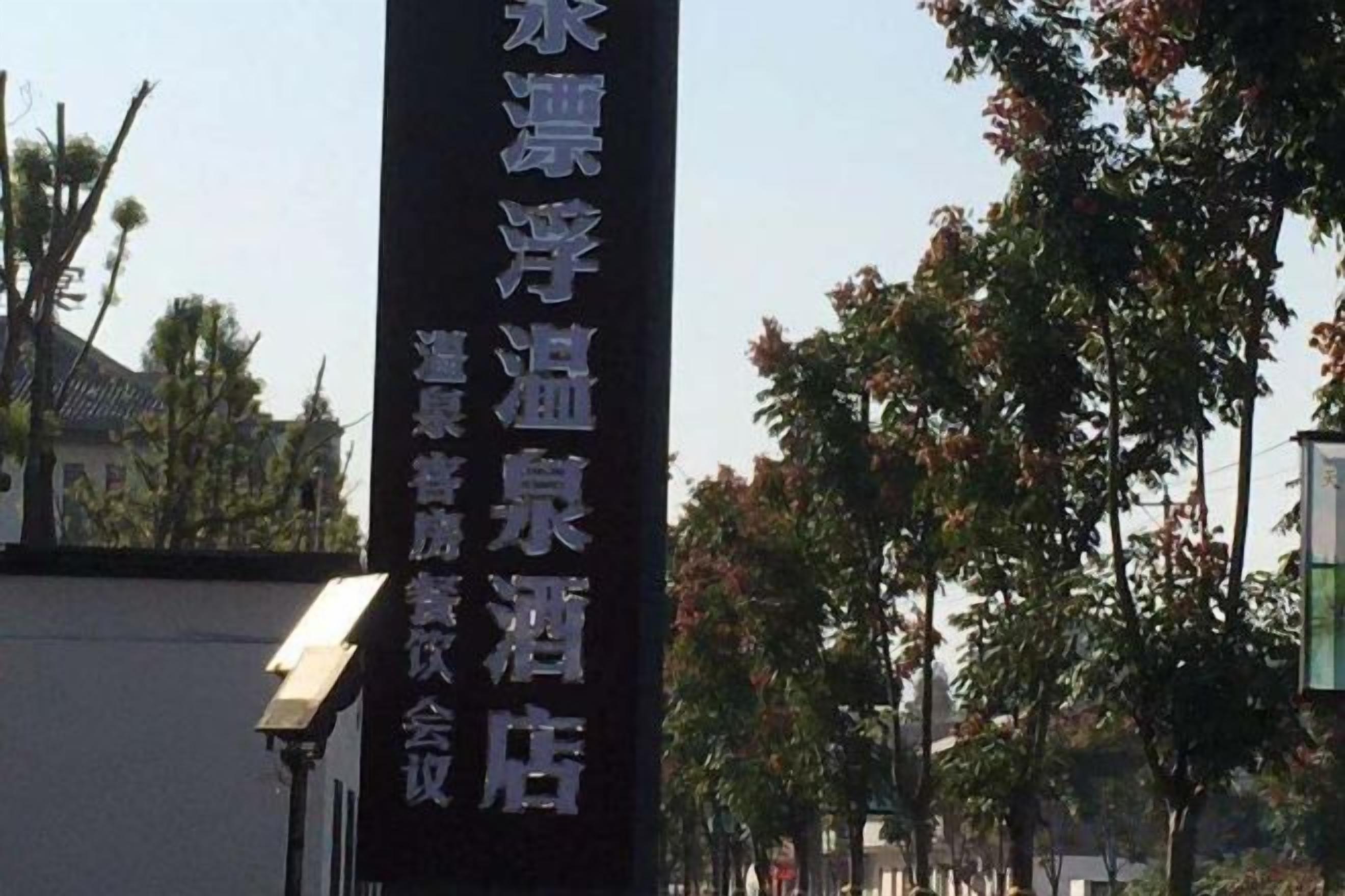 A vertical sign with text, likely indicating a hotel or establishment name, set against a backdrop of trees and a building.