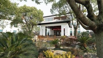 A traditional building with a covered entrance, surrounded by lush greenery and a small pond.