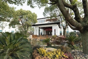 A traditional building with a covered entrance, surrounded by lush greenery and a small pond.