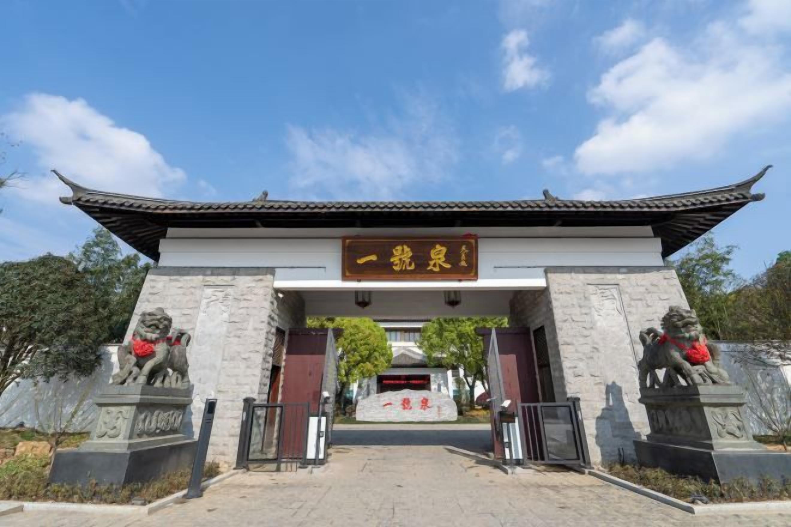 Une porte chinoise traditionnelle, flanquée de statues de lions en pierre de chaque côté, un ciel d’un bleu limpide et une enseigne avec des caractères chinois.