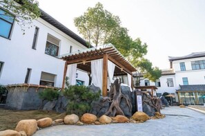 Een traditionele Japanse houten gazebo met een rotstuin en een boom voor een modern gebouw.