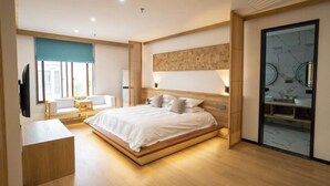 A modern hotel room with a large bed, a desk, a chair, and a bathroom with a glass shower. - Yihaoquan Piaofu Hot Spring Hotel (Lujiang)