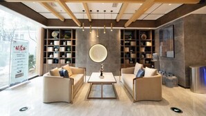 A modern hotel lobby with a central seating area, wooden ceiling beams, and a large circular wall decoration. - Yihaoquan Piaofu Hot Spring Hotel (Lujiang)
