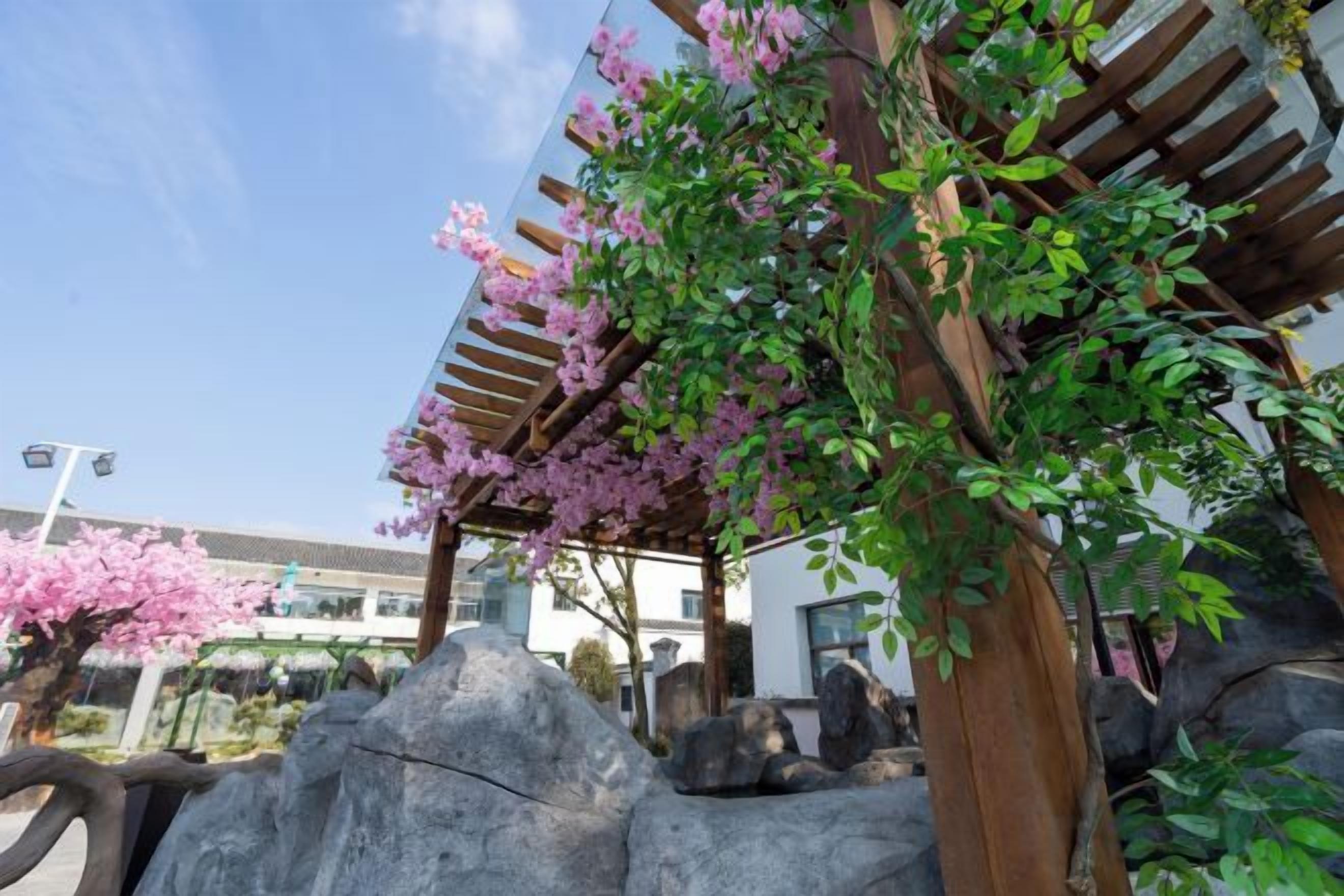 A covered outdoor area with a pergola, large rocks, and flowering plants.