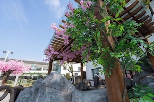 Un espacio exterior cubierto con una pérgola, grandes rocas y plantas con flores.