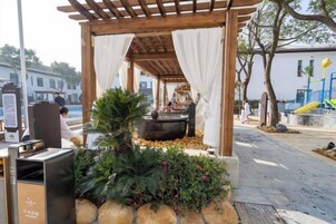 Un espacio de estar al aire libre cubierto con una jardinera de piedra, una fuente de agua y una pérgola con cortinas blancas.