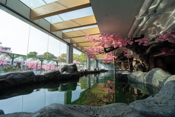 An indoor garden with a water feature, rocks, and cherry blossoms. - Yihaoquan Piaofu Hot Spring Hotel (Lujiang)