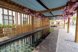 Un pasillo con una fuente de agua reflectante, columnas de madera y un paseo cubierto.