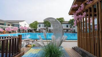 A swimming pool with a wooden deck, a decorative metal sculpture, and a building with pink flowers.