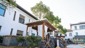 A courtyard with a wooden pergola, rock formations, and a white building with windows. - Yihaoquan Piaofu Hot Spring Hotel (Lujiang)