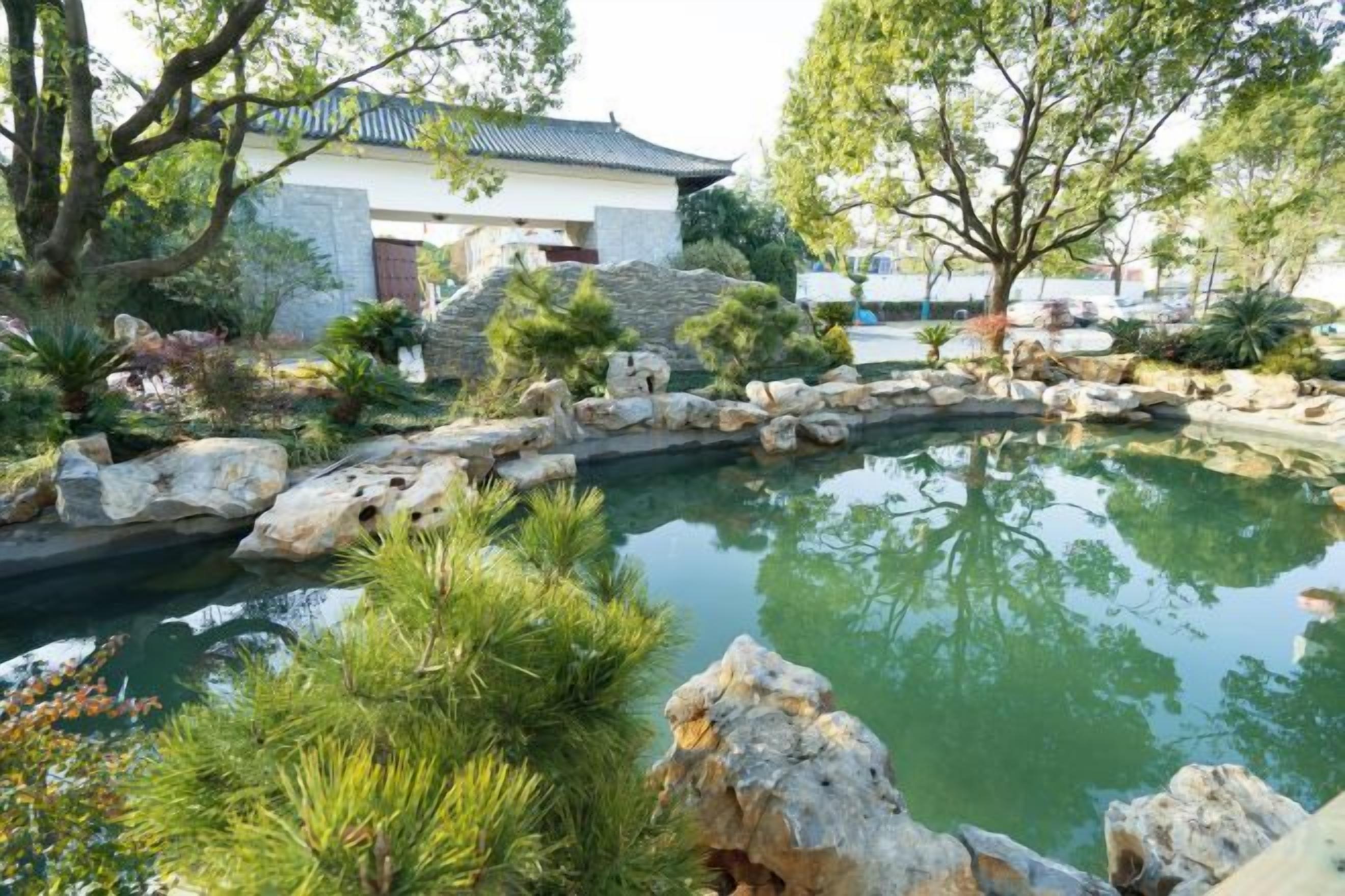 A tranquil garden with a pond, rocks, and a building with a tiled roof.