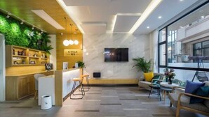 A modern reception area with a wooden counter, bar stools, a TV, and a seating area with a sofa and chairs. - Shengsiya home stay (Shengsi)