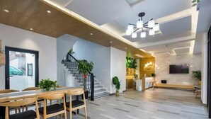 A modern hotel lobby with a wooden dining table, chairs, a staircase, and a reception desk. - Shengsiya home stay (Shengsi)