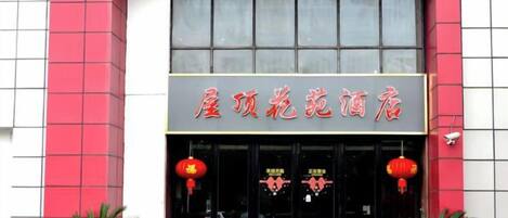 A hotel entrance with a sign in Chinese characters, two red lanterns, and potted plants.