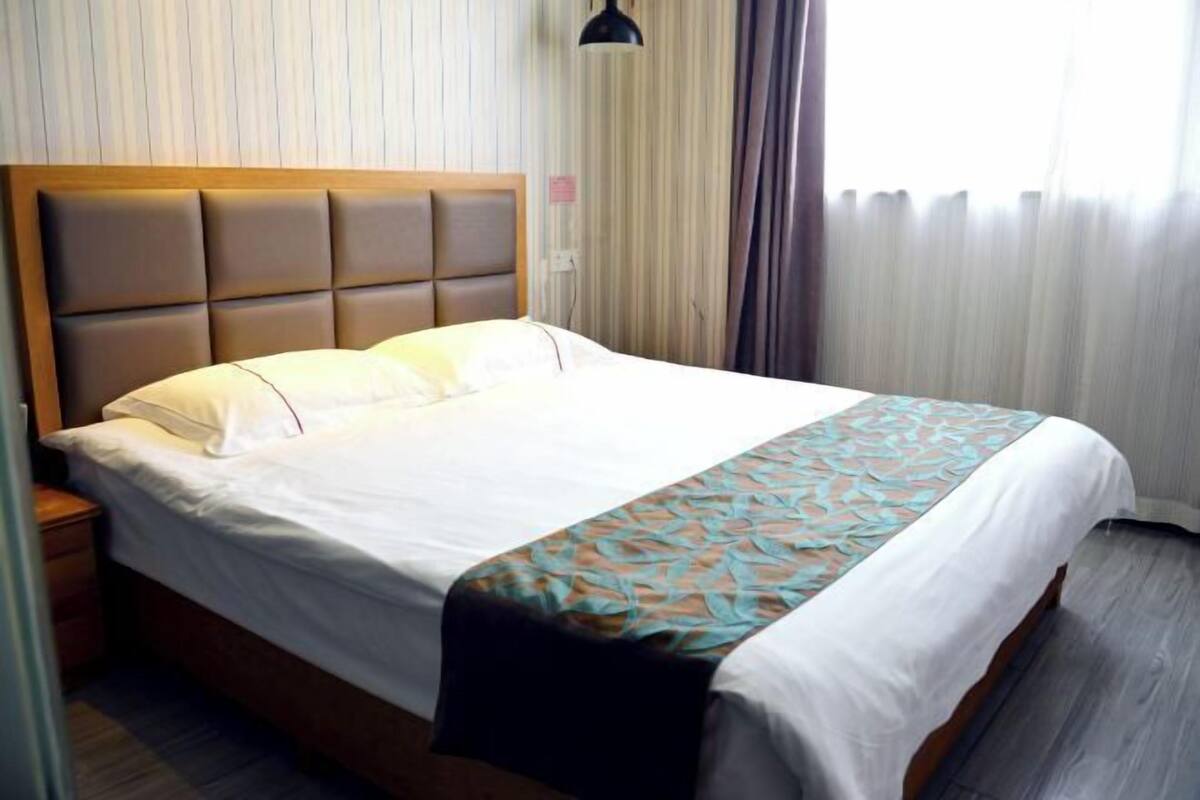 Une chambre d’hôtel avec un lit, une table de chevet, une lampe et une fenêtre avec des rideaux.