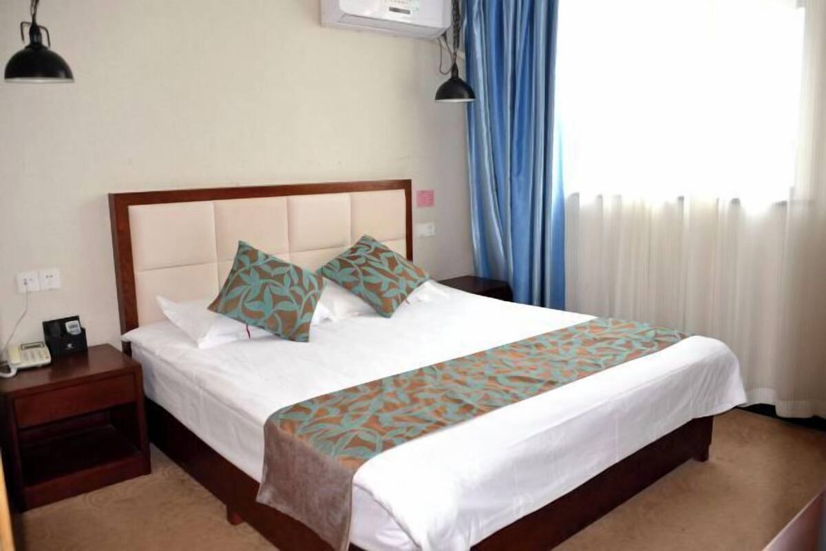 Une chambre d’hôtel comprenant un lit, une table de chevet, une lampe, un climatiseur et des rideaux.