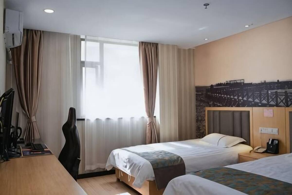 Une chambre d’hôtel avec deux lits, un bureau, une chaise et une grande fenêtre avec des rideaux.