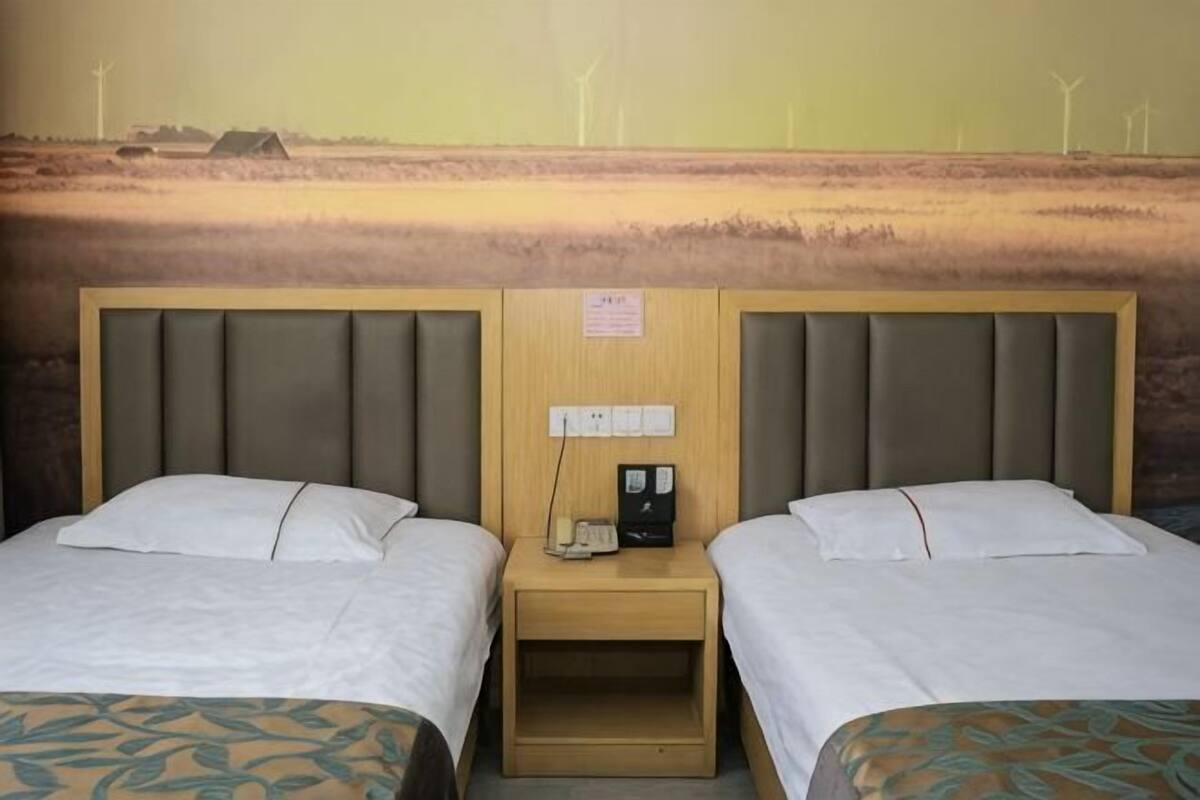 Une chambre d’hôtel avec deux lits, une tête de lit en bois, une table de chevet avec un téléphone et une vue sur des éoliennes.