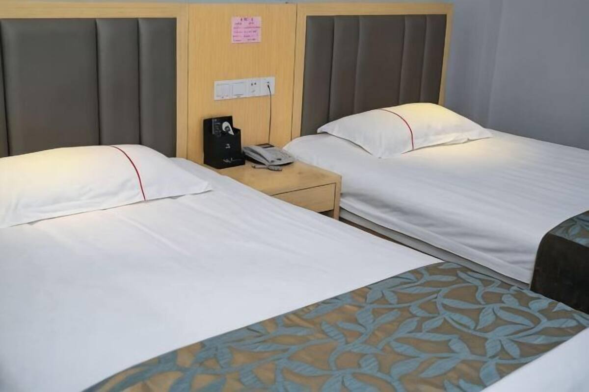 Une chambre d’hôtel avec deux lits, une tête de lit en bois, une table de chevet avec un téléphone et un interrupteur fixé au mur.