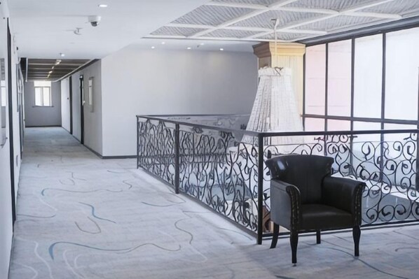 A corridor with a patterned floor, a black chair, and a railing with decorative metalwork. - Pudding hotel (Shanghai Chongming Dongtan store) (Shanghai)