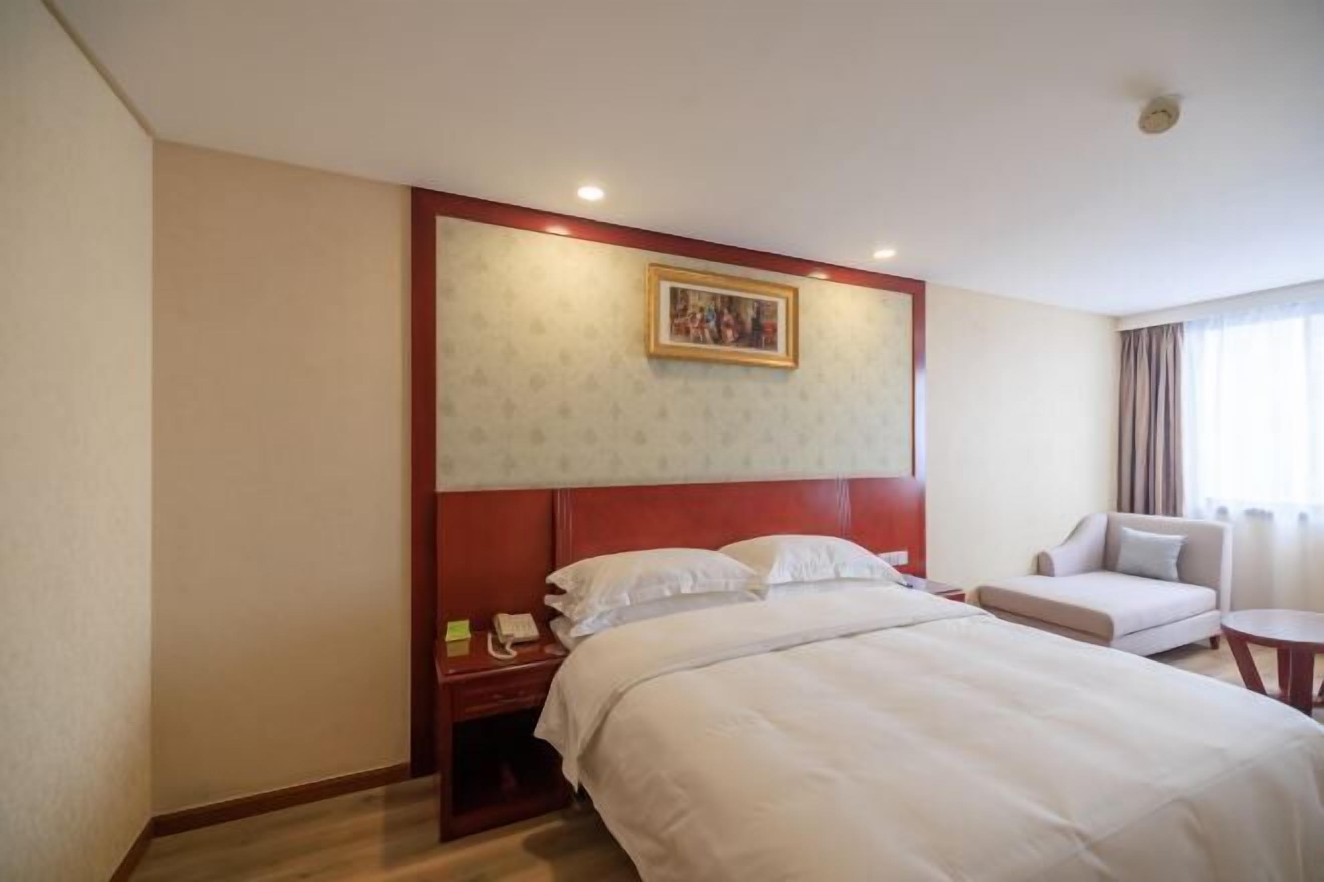 A hotel room with a large bed, a bedside table with a phone, a chair, and a window with curtains.
