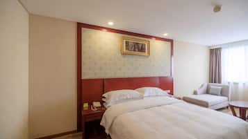 A hotel room with a large bed, a bedside table with a phone, a chair, and a window with curtains.