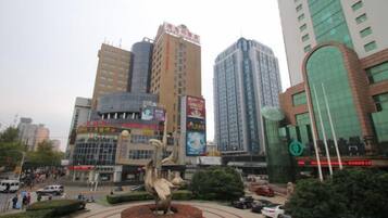 A cityscape with a central roundabout, a prominent sculpture, and tall buildings with commercial signage.