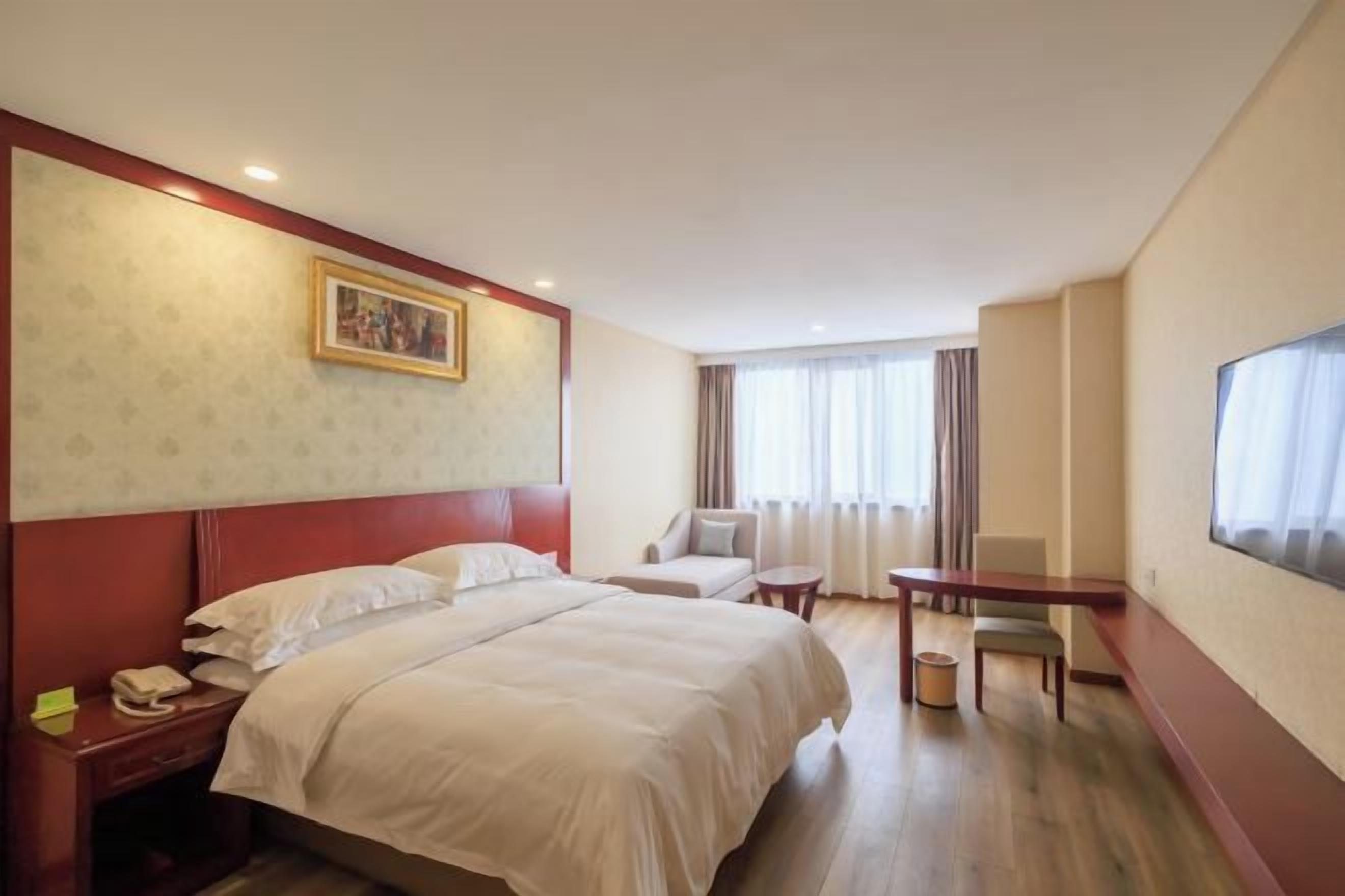 A hotel room with a bed, a desk, a chair, a small table, a TV, and a painting on the wall.