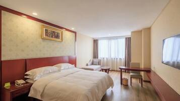 A hotel room with a bed, a desk, a chair, a small table, a TV, and a painting on the wall.