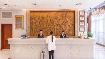 A reception desk with three staff members, a large wall sculpture, and a potted plant.