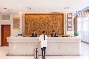 A reception desk with three staff members, a large wall sculpture, and a potted plant. - Vienna Hotel (Songbin Road Metro Station, Baoshan) (Shanghai)