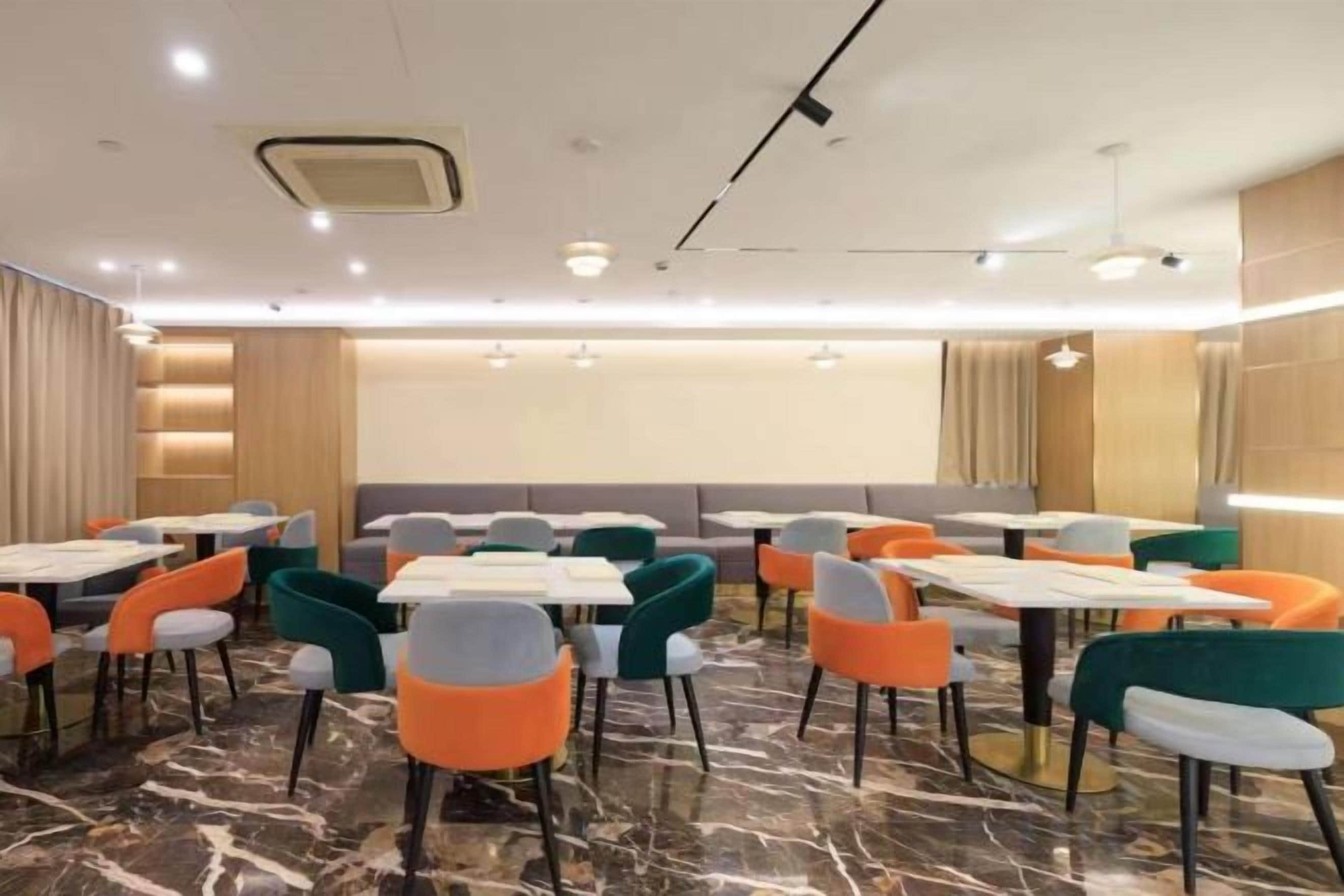 A hotel dining area with tables and chairs, a marble floor, and a large screen.