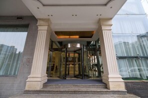 Een hotelingang met een draaideur, trappen en een glazen gevel.