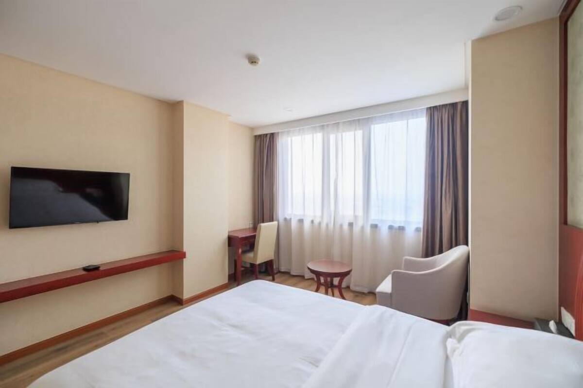 Une chambre d’hôtel avec un grand lit, un téléviseur fixé au mur, un bureau avec une chaise et une fenêtre avec des rideaux.