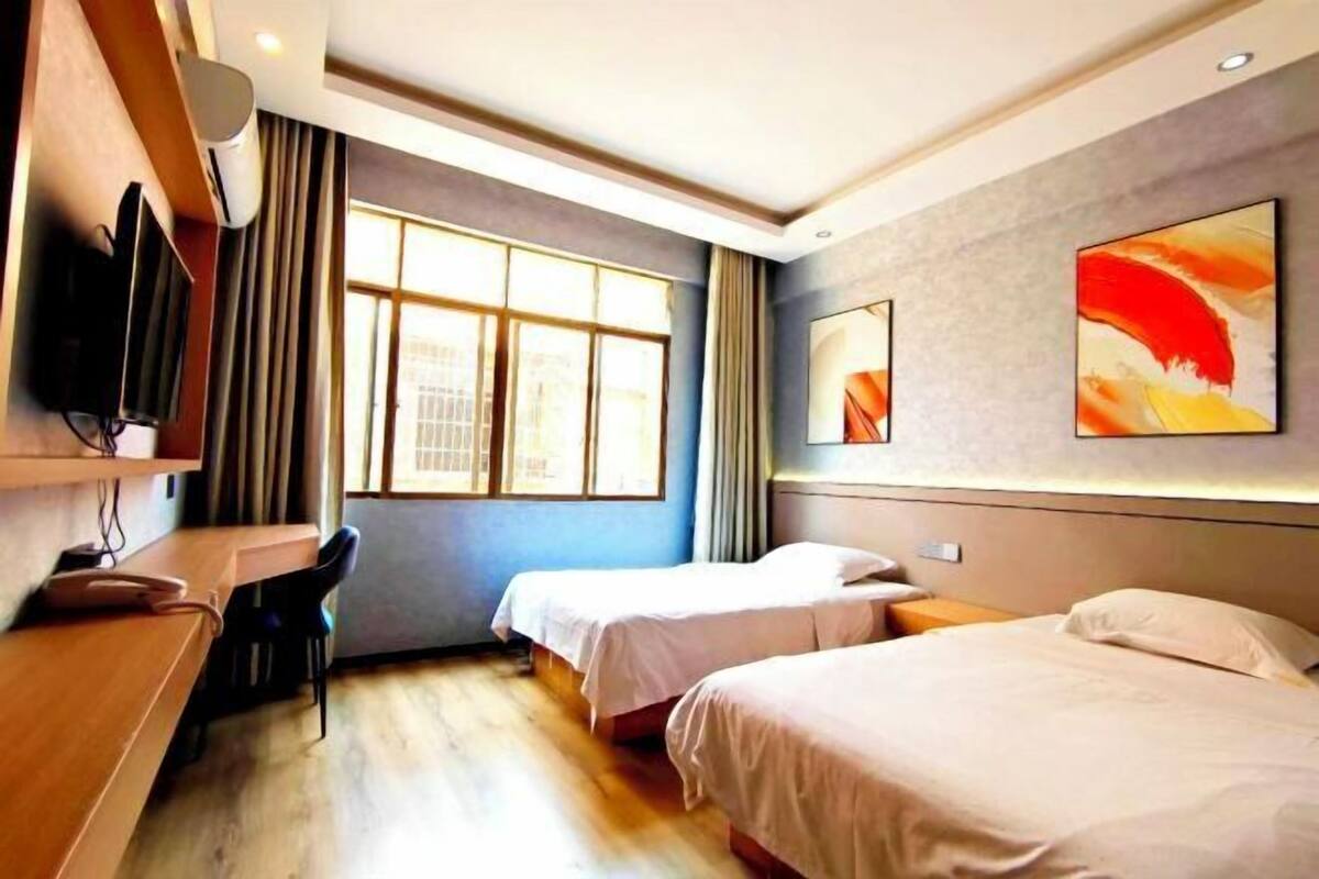 A hotel room with two beds, a desk, a chair, a TV, and a large window.