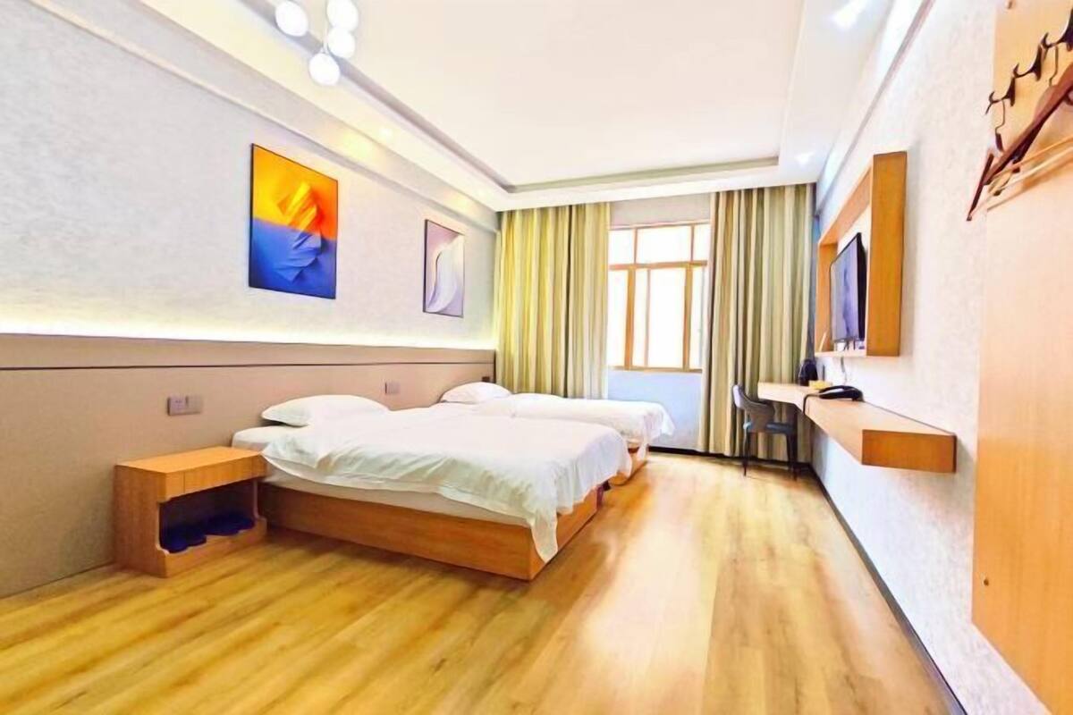 A hotel room with two beds, a wooden floor, a TV, and a desk.