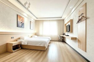 Una habitación de hotel moderna con piso de madera, dos camas, un escritorio, un televisor y un ventanal con cortinas.
