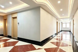 A hotel corridor with a marble floor, doors, and recessed lighting.