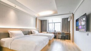 Ein Hotelzimmer mit zwei Betten, einem Schreibtisch, einem Stuhl, einem Fernseher und einem Fenster mit Vorhängen.