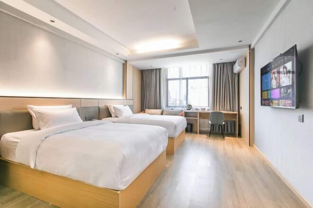 Habitació d'hotel amb dos llits, una taula de treball, una cadira, un televisor i una finestra amb cortines.