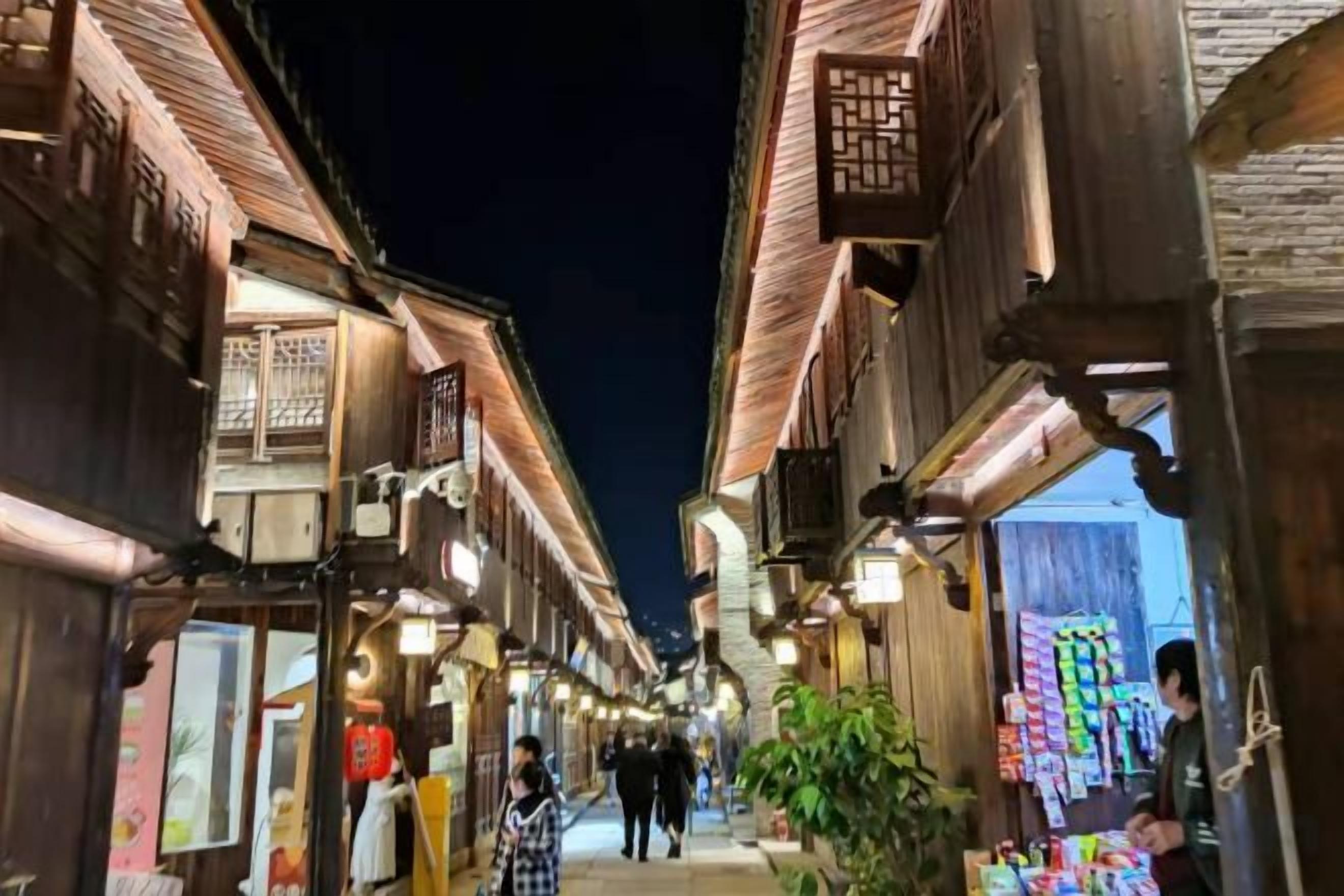 A narrow street with traditional wooden buildings, some with visible signage and awnings.