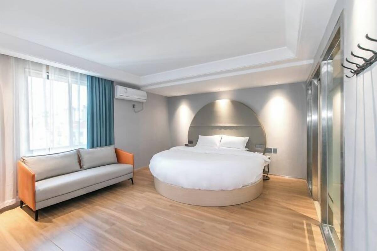 Habitació d'hotel moderna amb un llit rodó, un sofà i una finestra gran amb cortines.